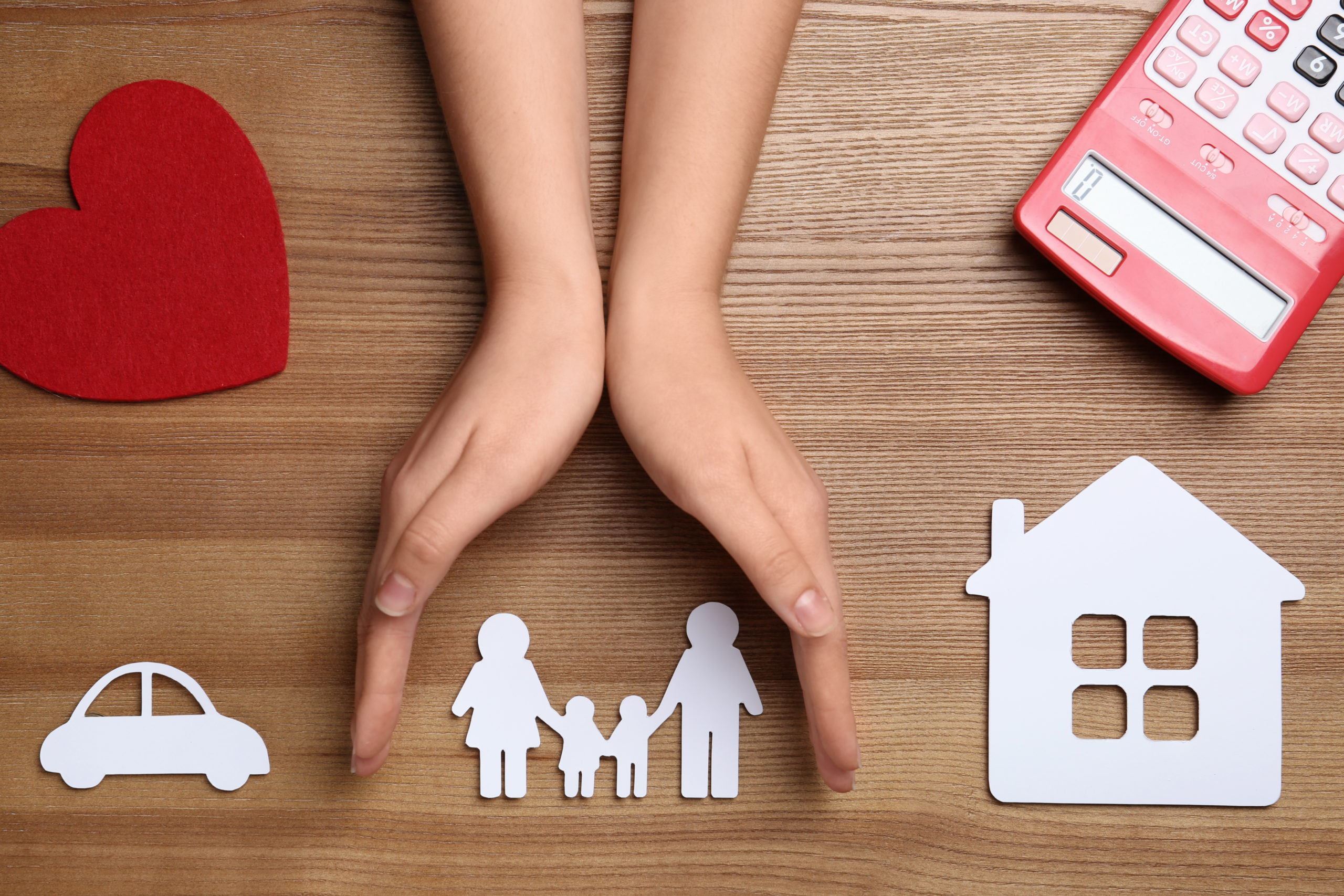 Woman holding hands over paper silhouette of family on wooden background, top view. Life insurance concept